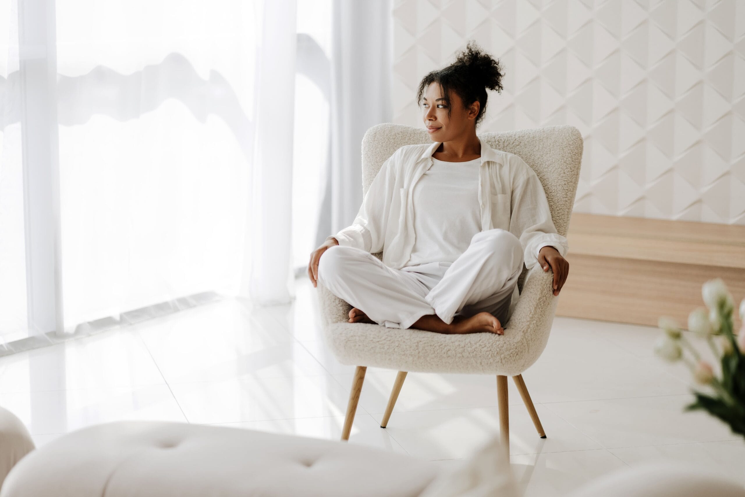 Jovem negra relaxando em casa sentada na poltrona no quarto branco. Síndrome dos ovários policísticos: O papel dos nutrientes no tratamento
