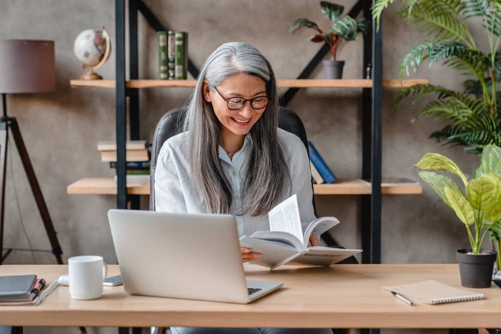Mulher sorrindo em um escritório ao ler um livro