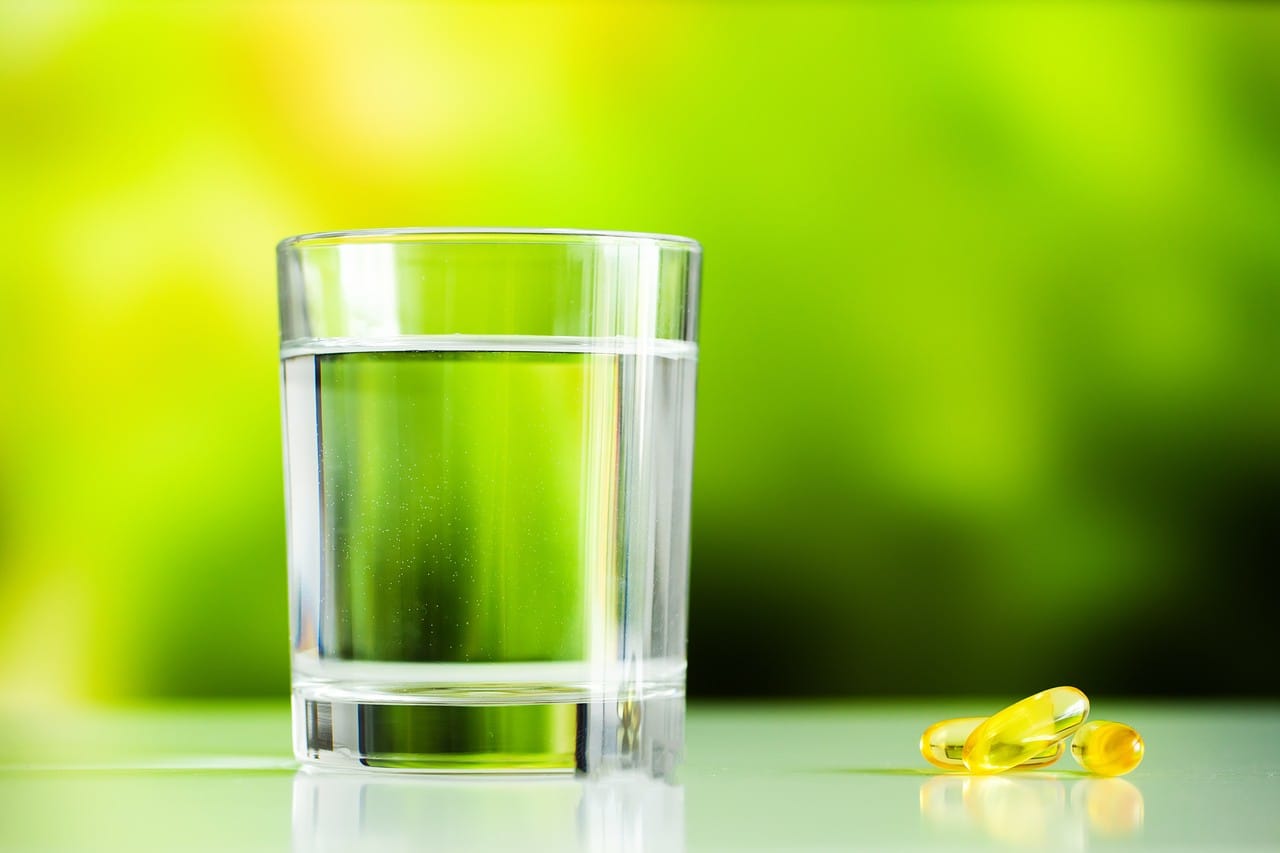 Copo de água com capsulas de omega 3 ao lado.