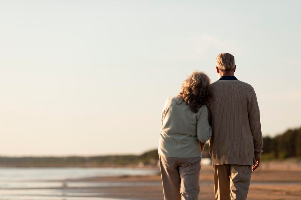 Casal idoso caminhando na praia ao pôr do sol