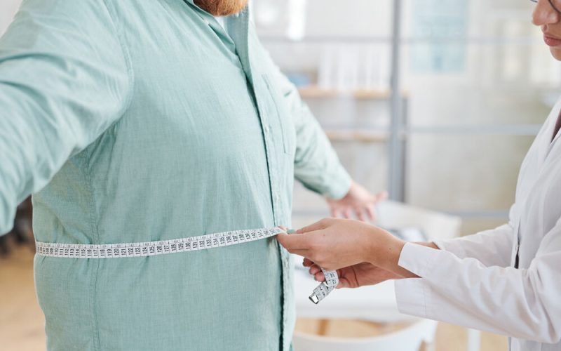 Close-up of doctor measuring waist of overweight man during his visit to the hospital