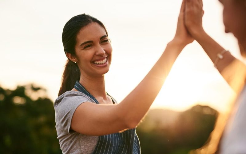 Mulher sorrindo e dando um high five ao entardecer