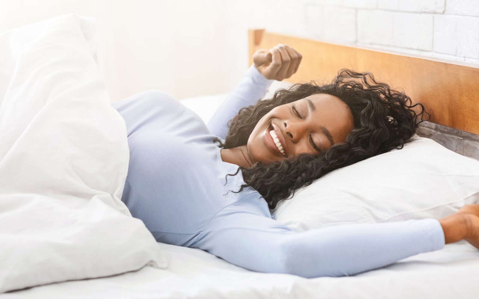 Young happy well-slept african woman stretching in bed, empty space, panorama