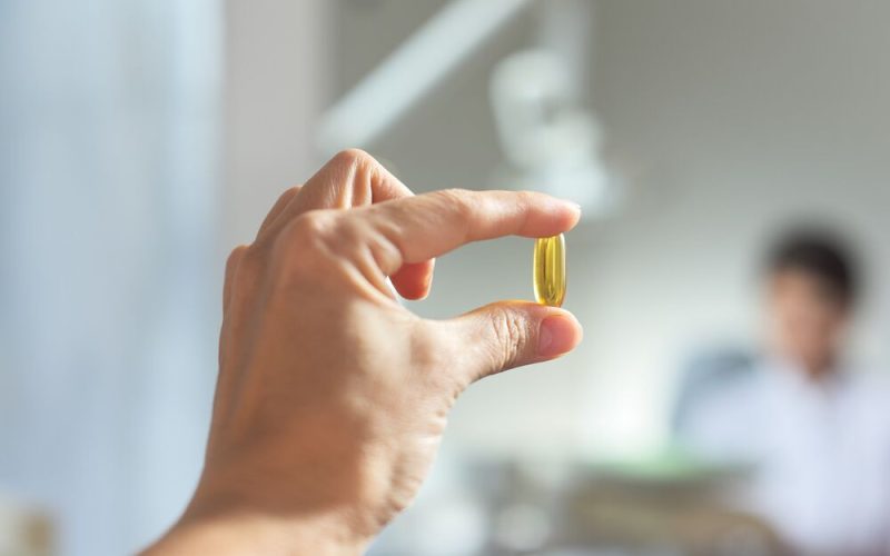 Yellow gel capsule of vitamin D, E, omega-3 in womans hand close-up